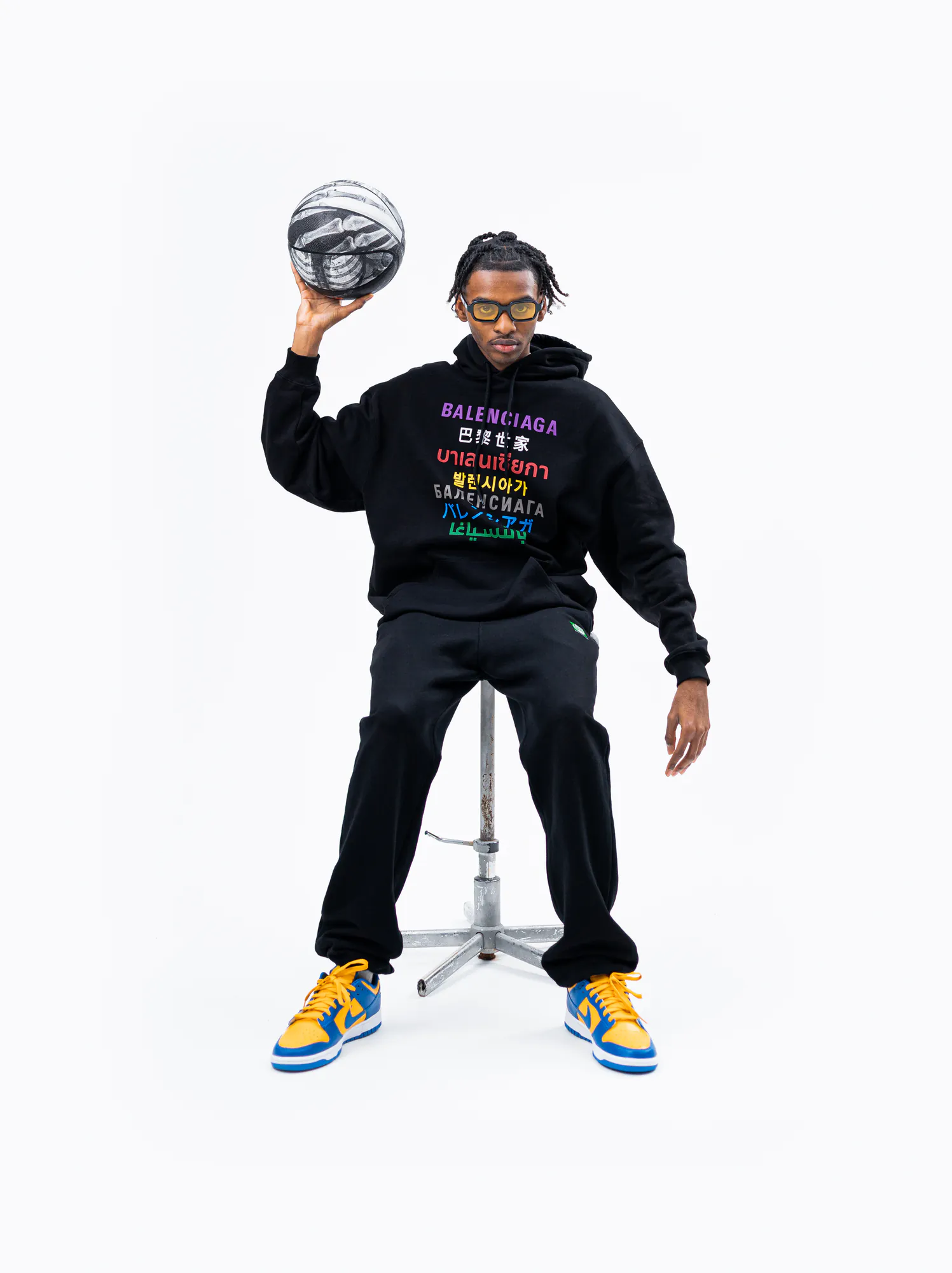 Modèle assis tenant un ballon de basket, hoodie graphique sur fond blanc