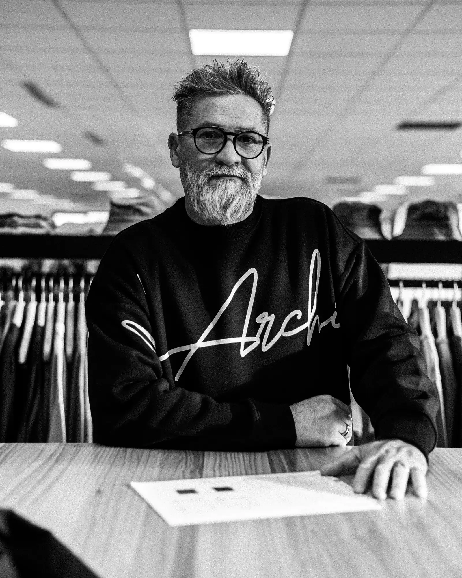 Portrait noir et blanc du fondateur au comptoir, hoodie floqué « Archi »
